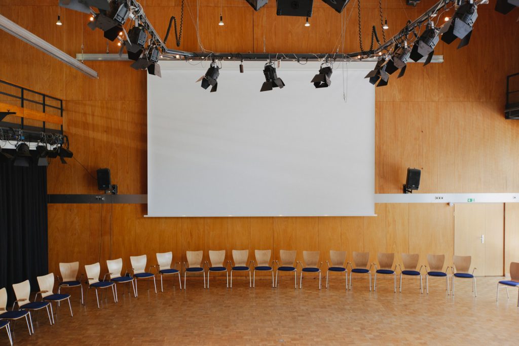 Stuhlhalbkreis vor heruntergefahrener Leinwand im Saal A der Akademie
